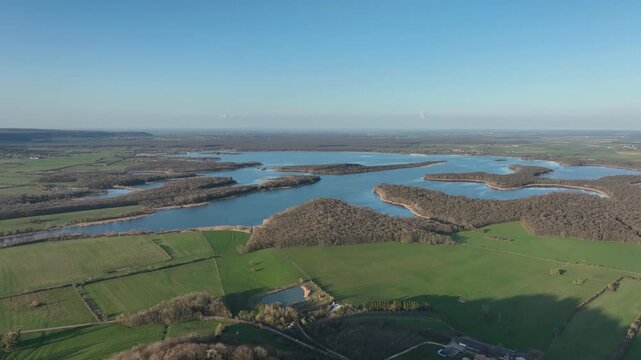 Aerial view of Lac de Madine in Meuse department with expansive blue lake forested islands green agricultural fields and distant horizon under clear blue sky