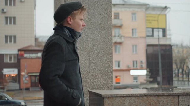 Young white creator leaning on railing overlooking city street filmmaker mapping storyboard poet composing lines photographer scouting angles soft drizzle reflective mood muted facades urban closeup