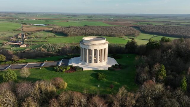 Aerial view of Butte de Montsec monument in Meuse department with classical colonnade on hilltop overlooking vast green fields and distant countryside under clear sky