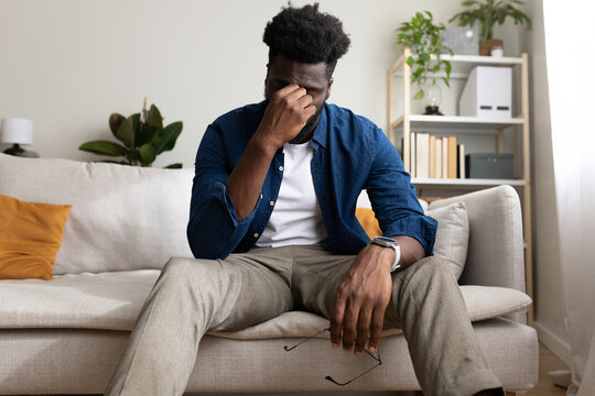 Tired Black man sitting on the sofa, having headache. Copy space.