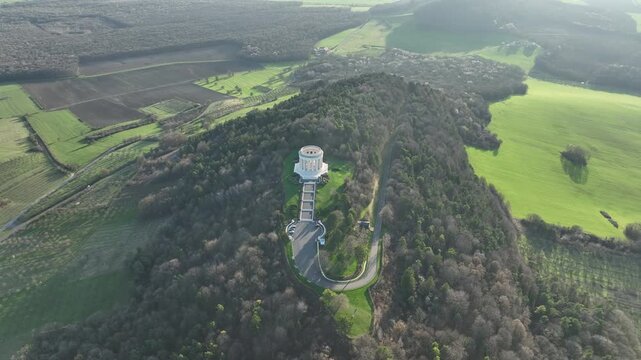 Aerial view of Butte de Montsec monument in Meuse department surrounded by dense forest with green fields roads and bright sunlight casting long shadows