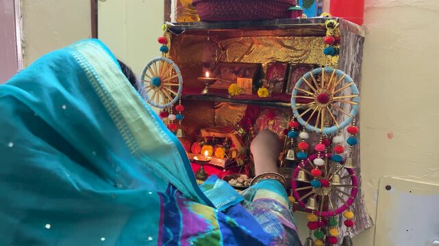 woman performing hindu home puja with diya and idols at decorated temple altar indoors