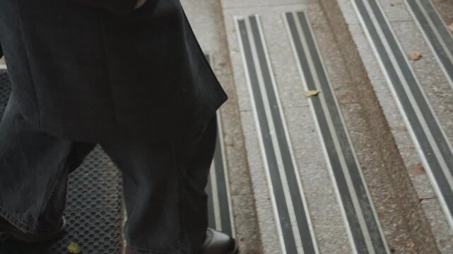 Closeup determined stride on steps, creator crossing threshold into foyer, wet grooves and metal nosing under leather boots, jeans sweeping, brisk purposeful movement, street to interior transition