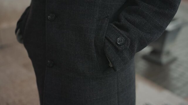 Black coat creator standing with hands in pockets, textured wool fabric, closeup of buttoned sleeve and cuff, cinematic urban sidewalk setting, subtle stillness suggests reflective creator preparing