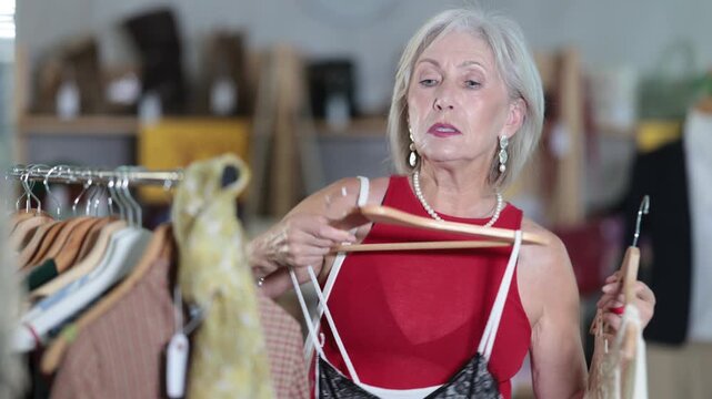 Woman chooses set of clothes for the summer. Visitor to the boutique examines the new summer collection of clothes