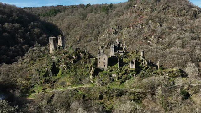 Aerial view of Tours de Merle medieval castle ruins with multiple stone towers on a forested hill in Correze valley