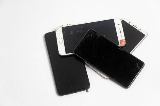 Pile of broken smartphones isolated on white background. Damaged mobile phones with cracked screen.