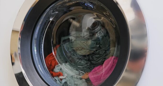 Close up video of a front loading washing machine drum spinning with colorful laundry in motion