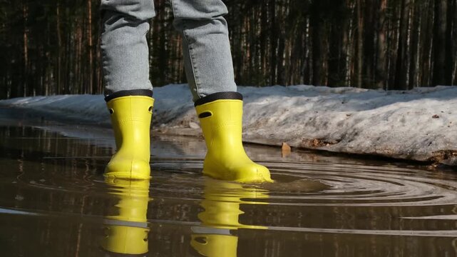 Child with yellow rain boots splattering muddy water in a big puddle, finding joy in outdoor spring season