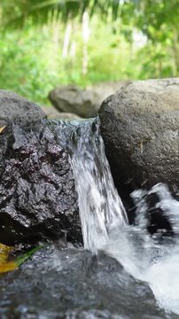 Tranquil Forest Waterfall Flowing Over Rocks With Soft Sunlight and Lush Greenery, peaceful nature vertical background. Flowing Mountain Stream Over Rocks Through Tropical Forest With Lush Green Folia