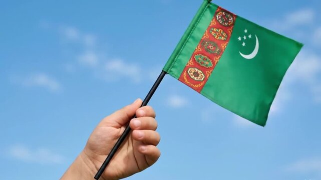 Child hand holding the Turkmenistan national flag against a bright blue sky for Independence Day or national celebration