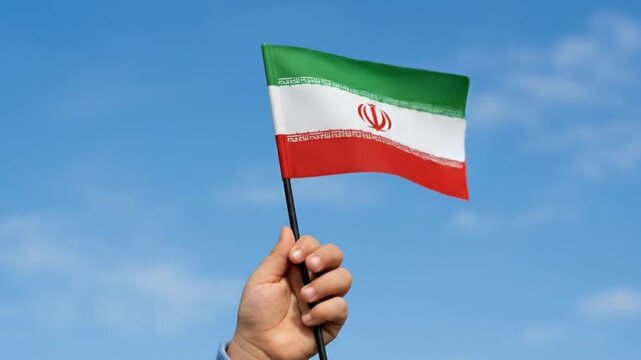 Child's Hand Holding Small Iranian Flag Waving Against Blue Sky