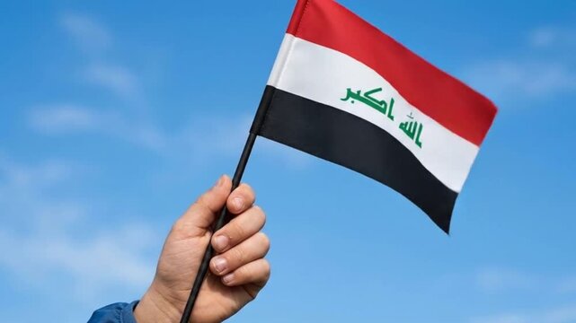 Small National Flag of Iraq Waving in Hand Against Blue Sky