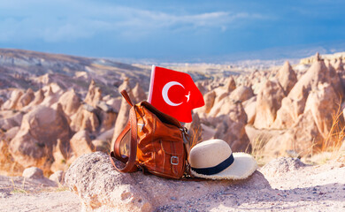 Obraz premium Traveler backpack with Turkish flag and straw hat overlooking fairy chimneys in Cappadocia, Turkey.