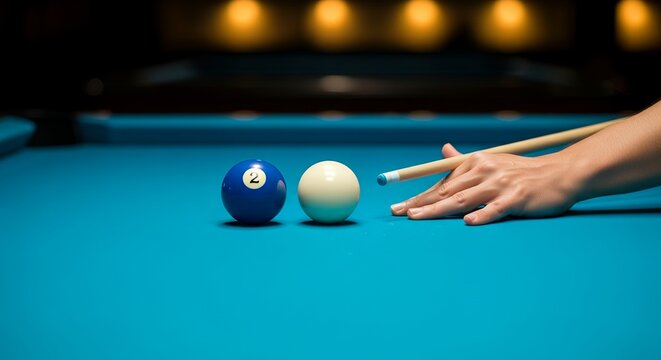 Hand holds cue near pool balls on blue table. Blue eight ball rests beside white cue ball. Fingers poised for shot, cue tip aligned. Warm lights glow softly behind pool table