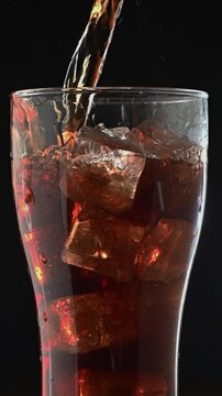 Close-Up of Sweet Soda Being Poured over Ice in a Tall Glass Extreme close-up of sweet soda being poured into a tall glass with ice cubes. Highlights the fizzy bubbles, texture of the liquid, and cond
