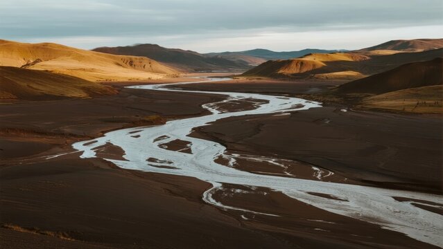 A winding river flows through a vast, arid desert landscape with rolling hills under a cloudy sky
