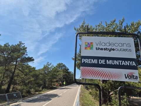 Volta Catalunya 2026 mountain points sign. A warning road sign stands against a green nature backdrop and a clear sky on a mountain travel route near. Photo taken on march 2026 near Prades, Catalunya.