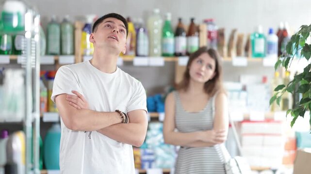 Young woman stands in a supermarket upset and resentful of a man who is standing in the background and talking emotionally. Couple quarrels in the hardware store