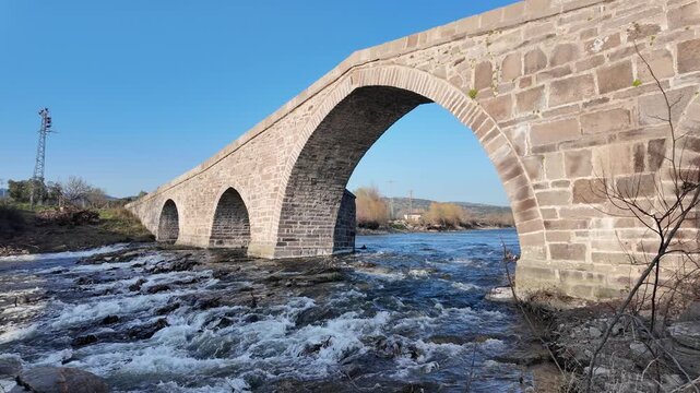 Ancient Stone Bridge over Tuzla Stream near Assos, Behramkale, Turkey Historical Ottoman Architecture and River Landscape at Sunset. High quality 4k footage