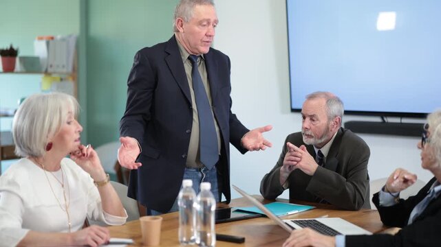 Irritated elderly male boss reprimanding upset subordinates sitting at table in office meeting room, expressing dissatisfaction with work. High quality 4k footage