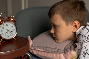 A nine-year-old boy has to get up early. He sleepily looking at his alarm clock.