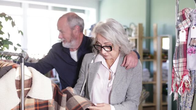  Mature couple spend time in shop and choose down jacket or checkered coat. Changing wardrobe, shaping style of clothing. Designer clothes, clothing of world brands