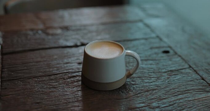 Handheld cinematic shot of a cup of latte on a rustic wooden table