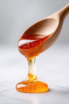 Viscous golden honey dripping from a wooden spoon onto a marble surface