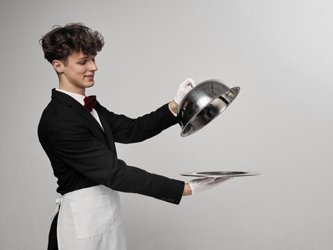 Waiter lifting cloche lid from tray in clean studio environment revealing serving gesture. Concept of food presentation, restaurant service, surprise reveal, dining experience.
