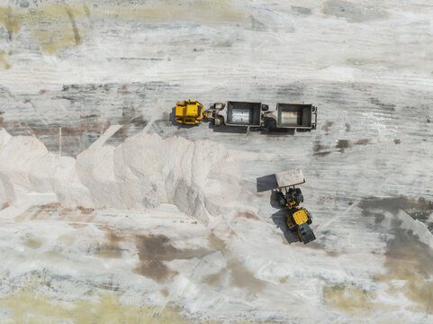 Aerial view of heavy machinery amidst the stark, white landscape of a salt processing area, creating a striking contrast with the yellow machinery, Walvis Bay, Erongo Region, Namibia.