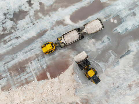 Aerial view of yellow machinery contrasting against pale salt flats, a stark industrial ballet unfolds, Walvis Bay, Erongo Region, Namibia.