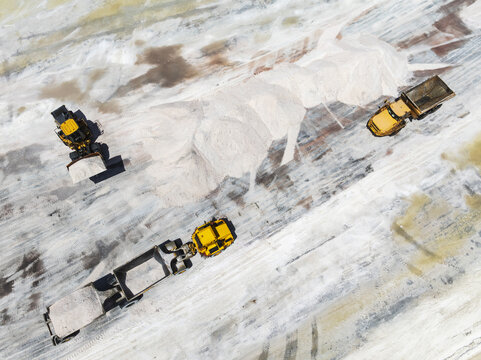 Aerial view of heavy machinery dwarfed by mountains of salt, the stark white contrasting against the pale earth, Walvis Bay, Erongo Region, Namibia.