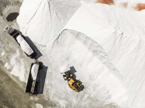 Aerial view of a stark, bright landscape where heavy machinery contrasts against the pure white piles of salt, a scene of industry carved into the earth, Walvis Bay, Erongo Region, Namibia.
