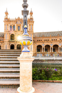 Travel, tourism: Ornate lamp post and architecture at Plaza de Espa&ntilde;a with sun flare, reflecting in the water, Seville, Spain.