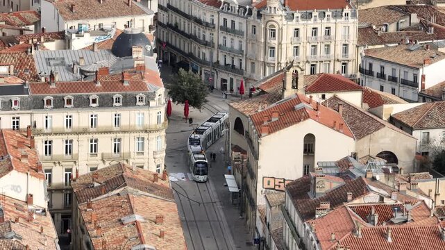 Aerial view of Montpellier dense urban street with tram on tracks surrounded by traditional buildings and rooftops under partly cloudy sky