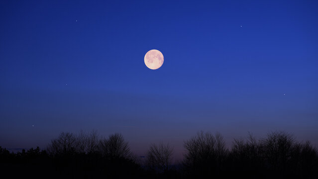 Full Moon, stars and planets above landscape silhouettes.
