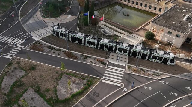 Aerial view of Montpellier tram on curved road near underpass with graffiti and surrounding greenery under daylight
