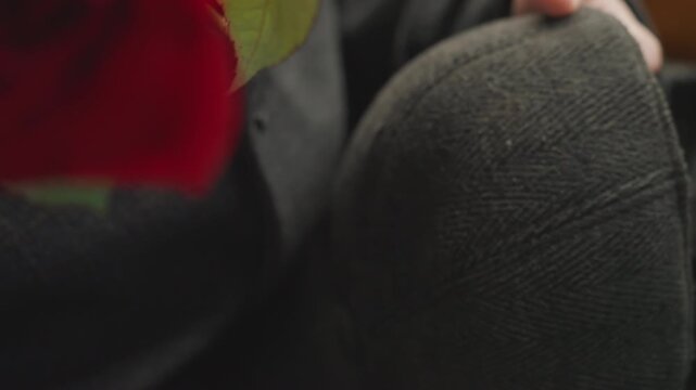 Intimate white creator adjusting wool hat, hands smoothing textured cap near blurred red rose, vintage coat sleeve, careful stitching and mending motion, tactile studio craft moment