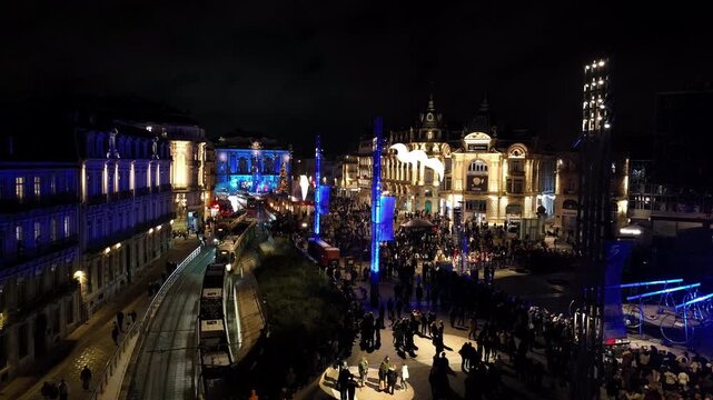 Night view of Montpellier place de la comedie bustling with crowd tram and blue light installations in front of grand buildings