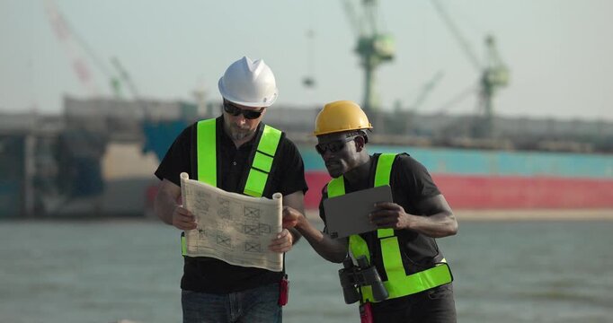 Engineer and technician review port operations and coastal logistics beside the waterfront in daylight, supporting maritime planning, cargo monitoring, and harbor infrastructure assessment.
