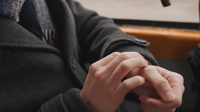 Creator hands clasped on bus seat, closeup of fingers fidgeting inside wool coat sleeve, button detail, window light, quiet commuter mood, planning next project with nervous energy