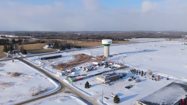 Industrial Factories Covered In Snow With The Town Of Erin Water Tower In Ontario, Canada, Aerial Orbiting Shot.