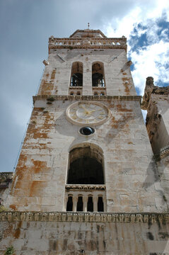 The historic stone bell tower of Saint Marks Cathedral in Korcula features a golden clock face and a black astronomical sphere above an arched opening