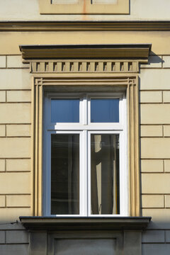 A white framed glass window set within a decorative beige stone facade featuring a detailed lintel and dentil molding