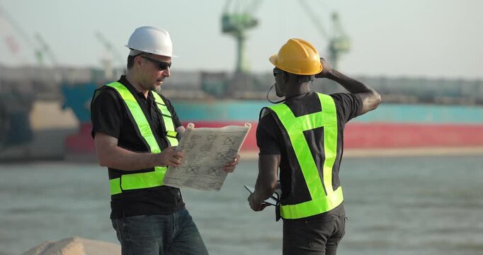 Engineer and technician review port operations and coastal logistics beside the waterfront in daylight, supporting maritime planning, cargo monitoring, and harbor infrastructure assessment.
