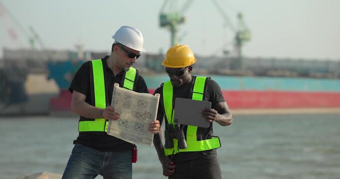 Engineer and technician review port operations and coastal logistics beside the waterfront in daylight, supporting maritime planning, cargo monitoring, and harbor infrastructure assessment.
