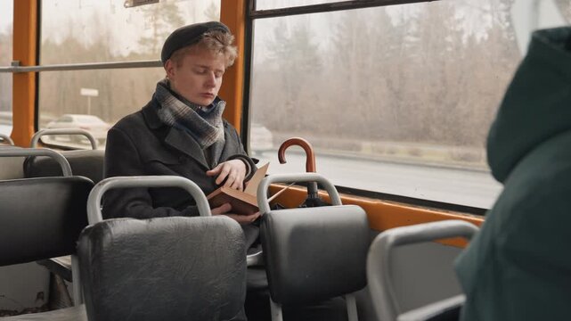 Young creator reading on bus, leather book open on lap, umbrella resting beside seat, wool scarf and coat, autumn window view, pensive expression, slow commute mood, indie creator moment