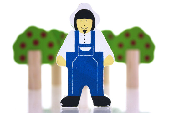 Toy farmer in front of toy trees on a white background