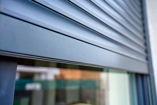 Close up of modern metal roller shutter partially covering window on building exterior. Concept of home security, privacy, protection and contemporary architecture.